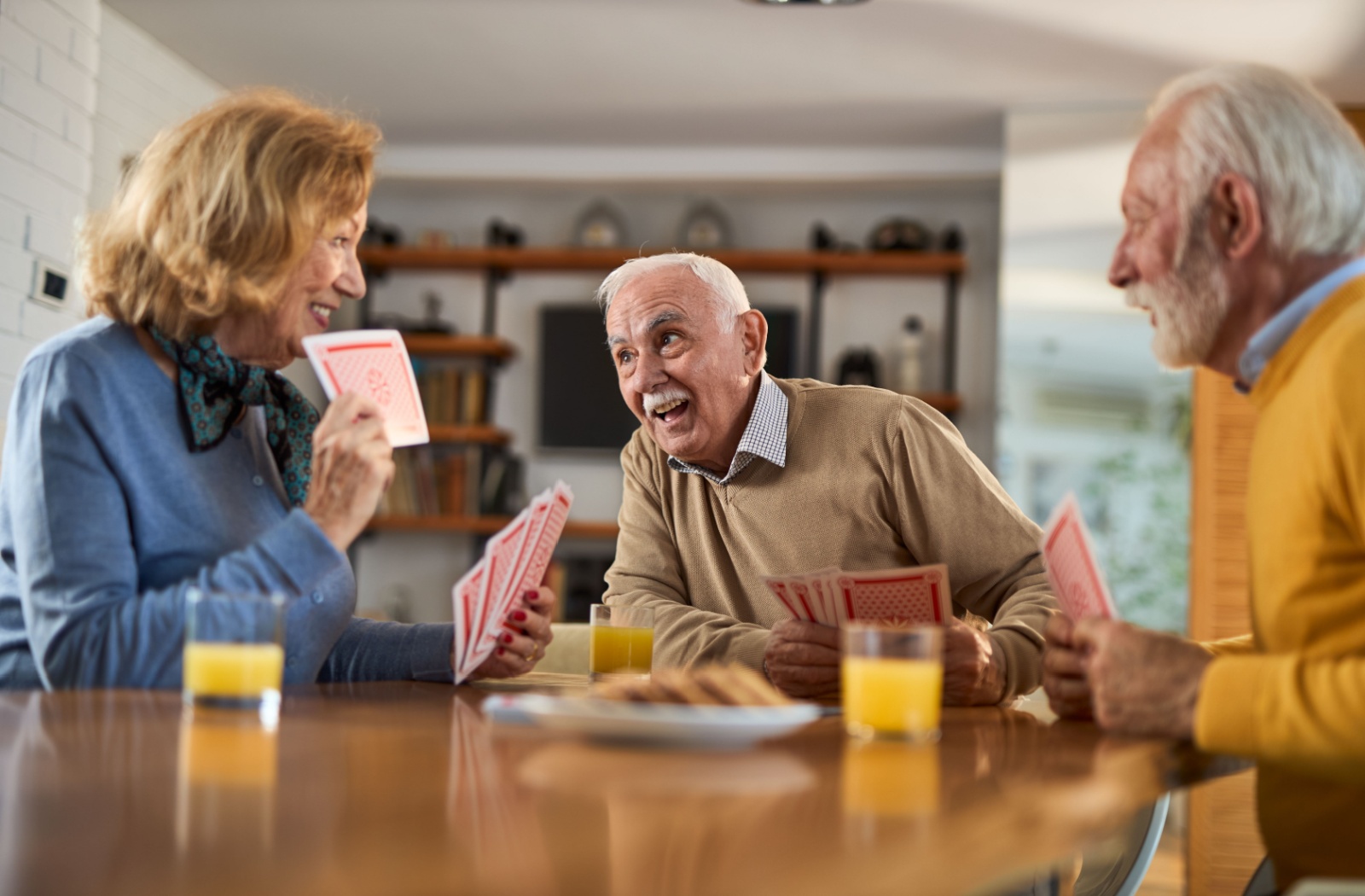 Three seniors laughing while having breakfast and playing cards in senior living.