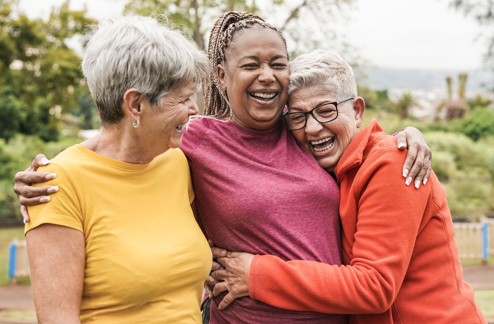 Three senior women in bright coloured tops hugging and smiling.