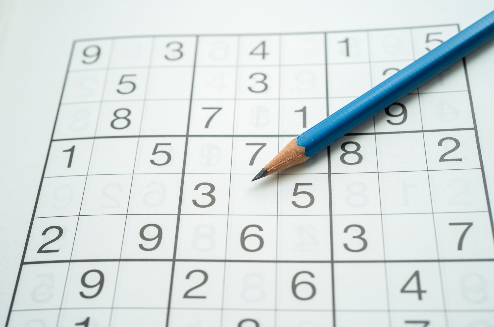 A close-up image of a page of sudoku with a sharpened blue pencil laying on top.
