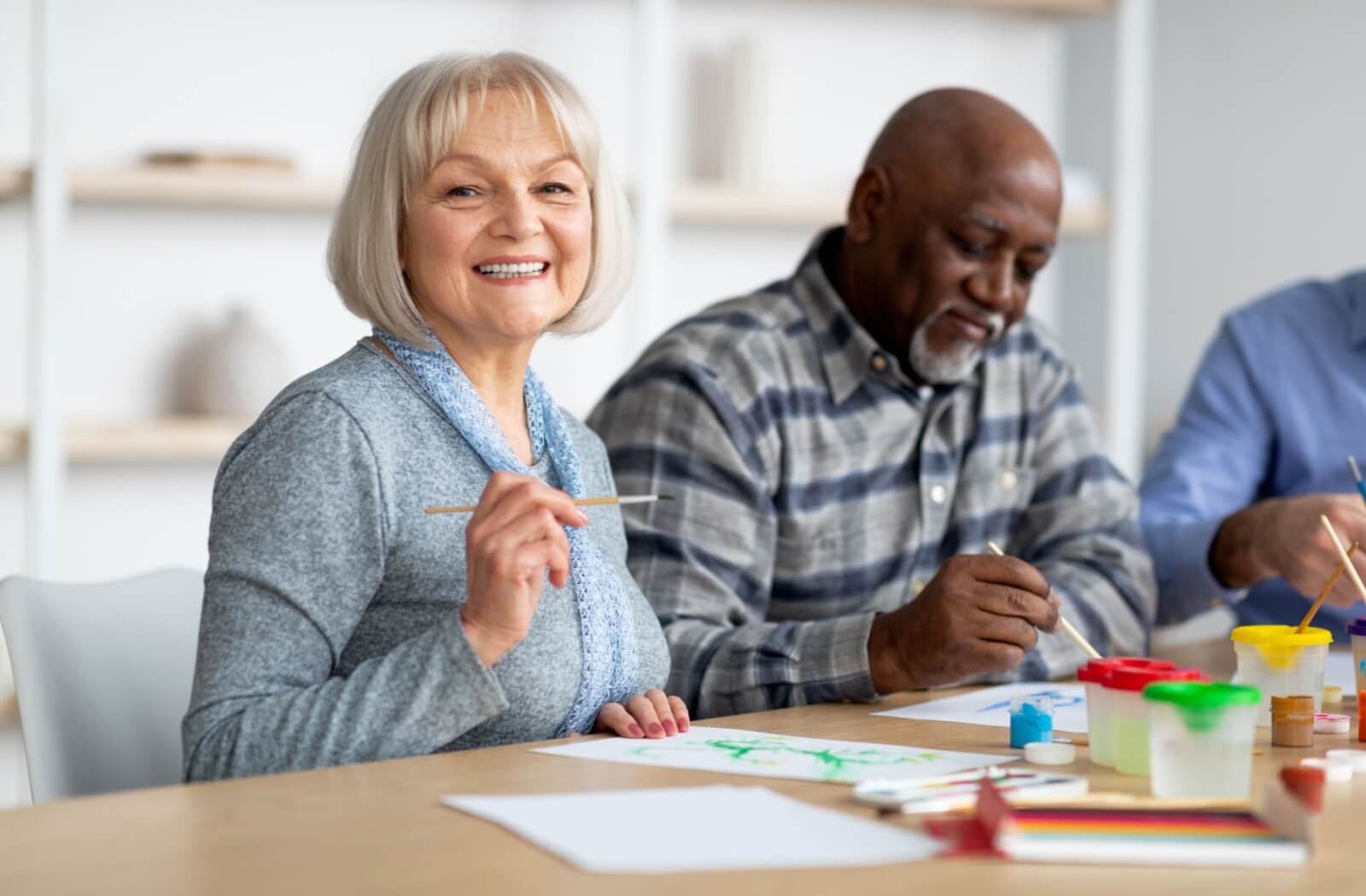 A smiling older adult painting with fellow residents in senior living.
