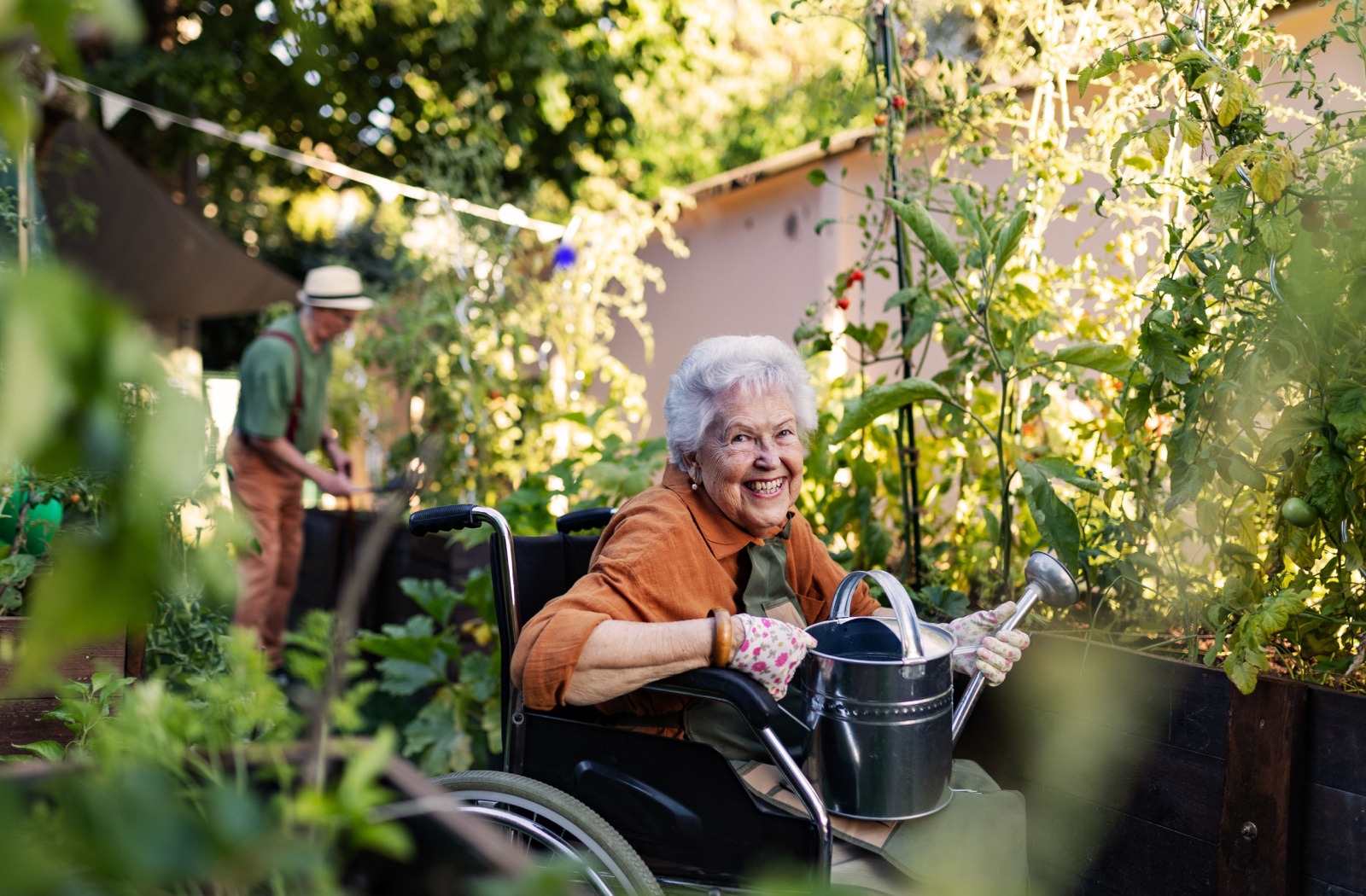 An older adult holding a watering can while tending to the community garden.