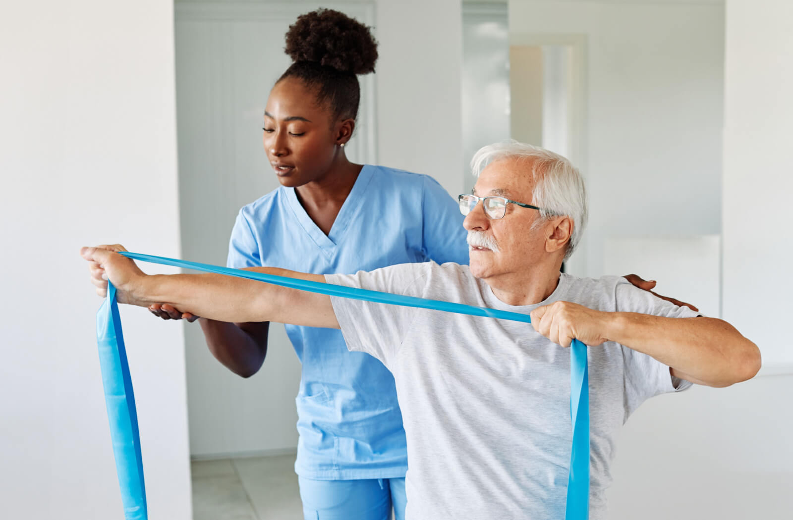 A caregiver in senior living helping an older resident use a resistance band to maintain muscle mass.