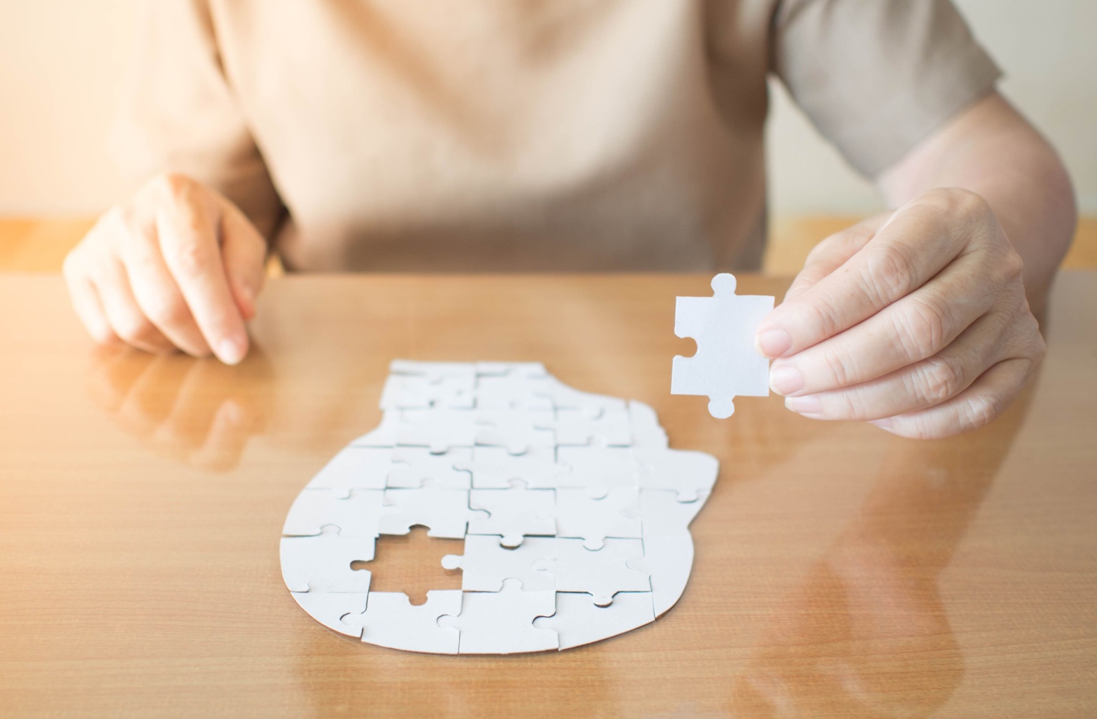 An older adult assembles a small white puzzle of the human head to strengthen their brain