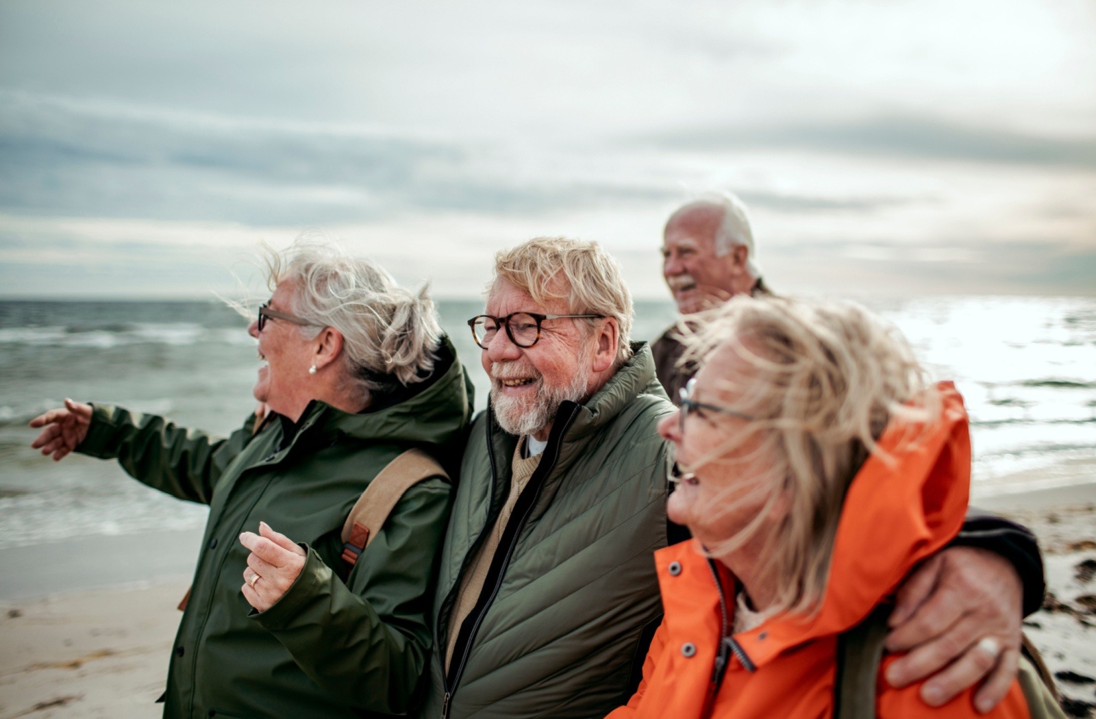 A group of senior friends smile and embrace each other while admiring a beach