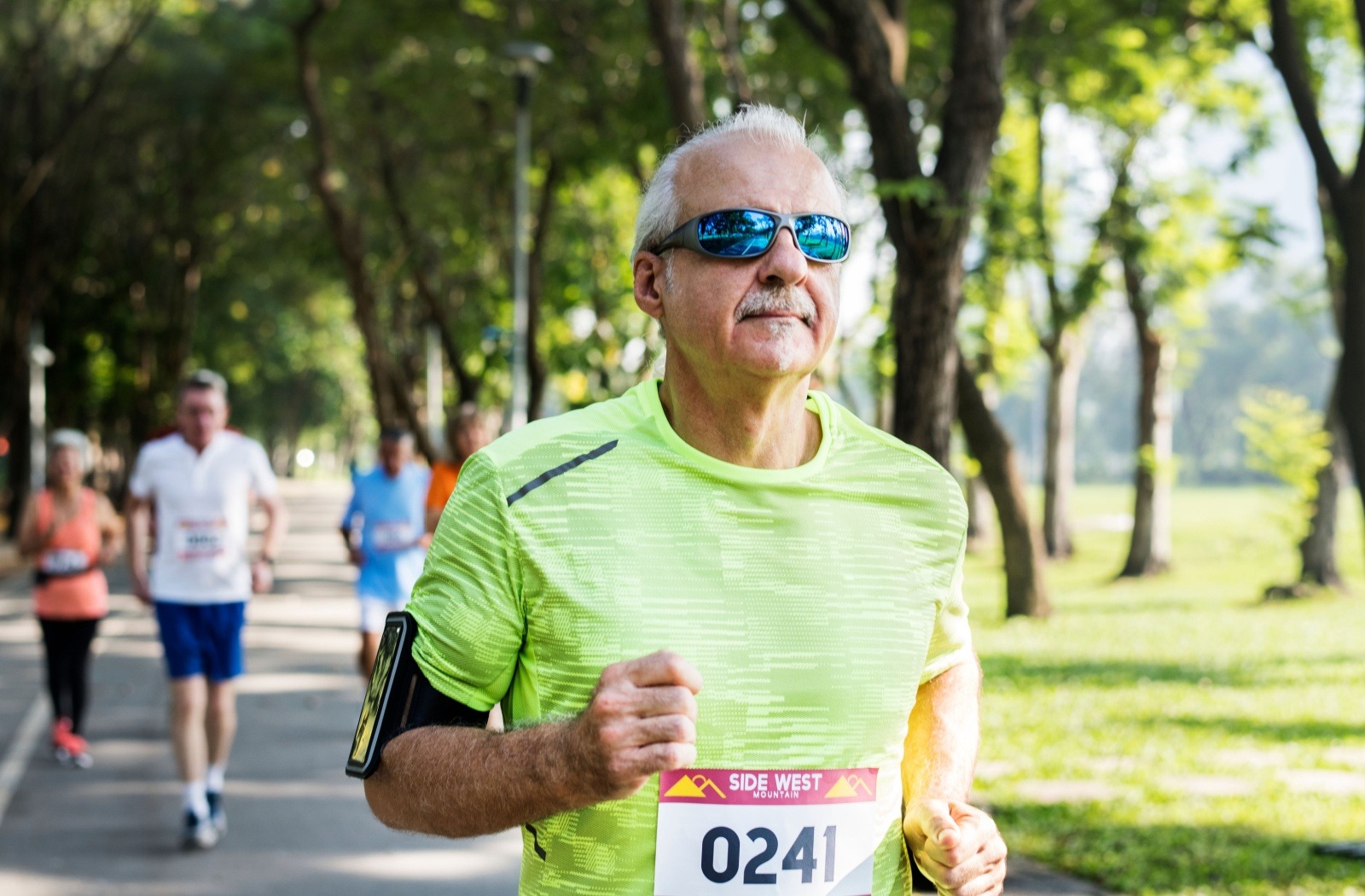 A senior in running gear and blue sunglasses runs in an organized race.